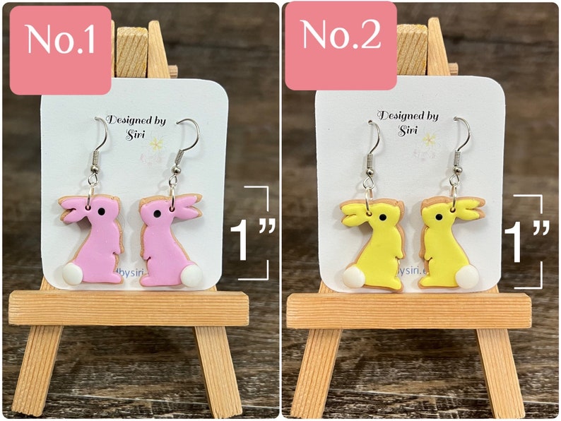 May include: Two pairs of polymer clay bunny earrings. The first pair is pink and the second pair is yellow. Each pair is 1 inch long. The earrings are on a white card with the text "Designed by Siri" and "@bysiri".
