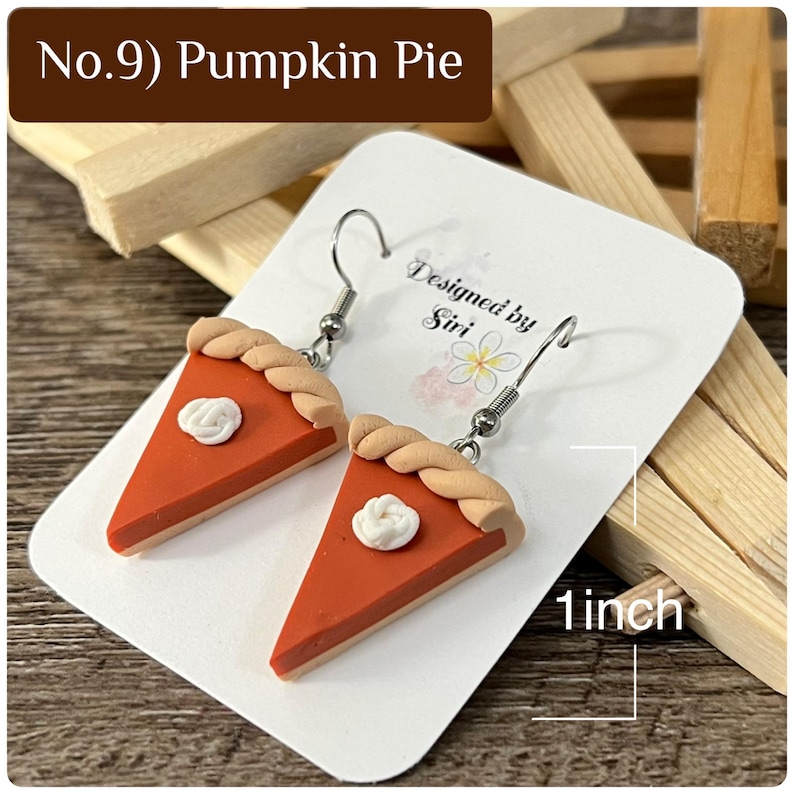 May include: A pair of pumpkin pie slice earrings with a tan crust, orange filling, and a white dollop of whipped cream. The earrings are displayed on a white card labeled No.9 Pumpkin Pie and Designed by Siri, showing a 1 inch measurement.