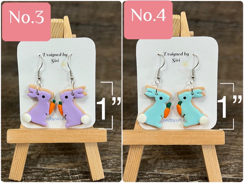 May include: Two pairs of dangle earrings featuring a bunny holding a carrot. The bunny on the left is purple and the bunny on the right is light blue. The earrings are 1 inch long. "Designed by Siri" is written on the card behind the earrings.