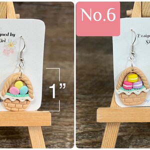May include: A pair of dangle earrings featuring a brown wicker basket filled with pastel colored eggs. The earrings are 1 inch long. "Designed by Siri" is written on the card behind the earrings.