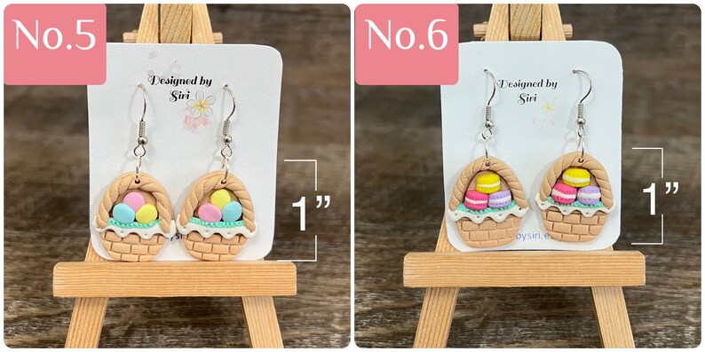 May include: A pair of dangle earrings featuring a brown wicker basket filled with pastel colored eggs. The earrings are 1 inch long. "Designed by Siri" is written on the card behind the earrings.
