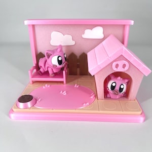 May include: A pink miniature pig scene with a pig on a bench, a pig in a house, and a pink oval rug. The scene includes a pink fence, white clouds, and a brown food bowl. The base is light tan.