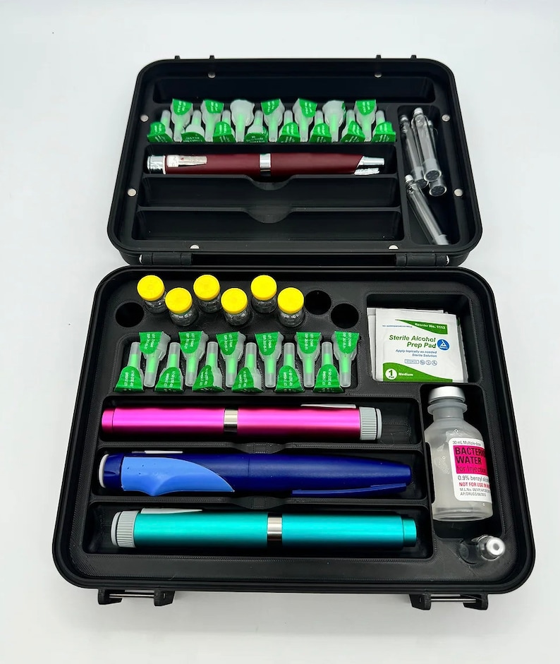 May include: A black hard-sided case with a foam insert for organizing medical supplies. The case contains vials, needles, a pen, alcohol prep pads, and a bottle of sterile water. The text on the bottle reads "Bacteriostatic Water".