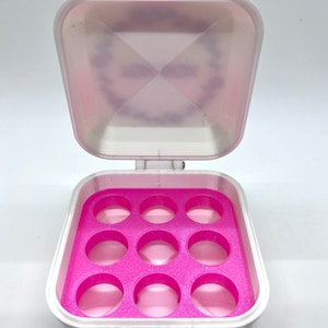 May include: A white plastic storage box with a pink lid and a pink interior. The box has 10 round compartments.