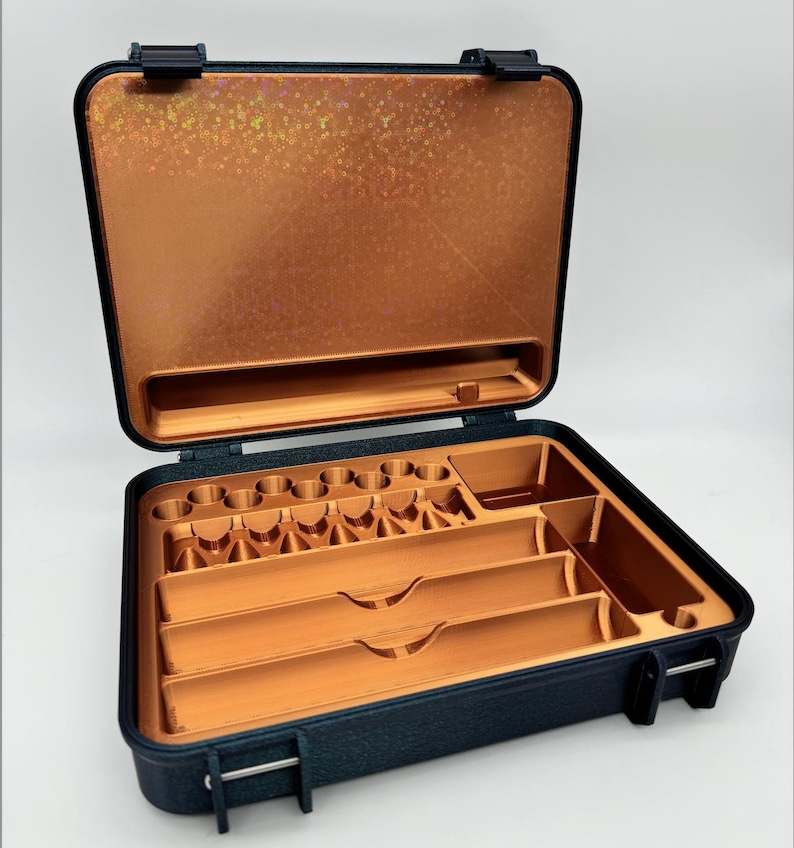 May include: A black hard-shell case with a copper-colored interior. The case has multiple compartments and slots for organizing small items. The lid of the case has a textured, iridescent surface.