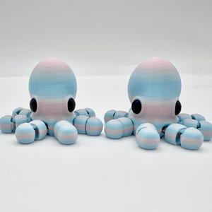 May include: Two 3D-printed octopus figurines. Each octopus has a rounded head and eight segmented tentacles. The heads are light blue and pink, with black eyes. The tentacles are light blue and pink striped. The figurines are on a white surface.