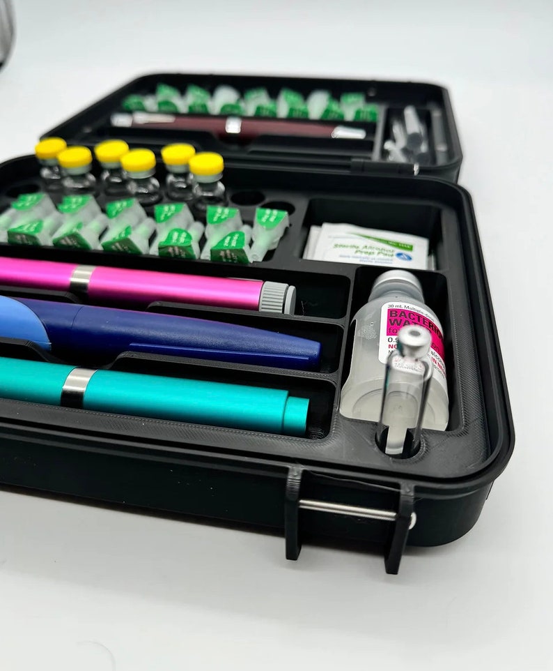 May include: A black plastic case with a variety of medical supplies, including vials, syringes, and a bottle of antibacterial wash. The case has a latch to keep it closed.