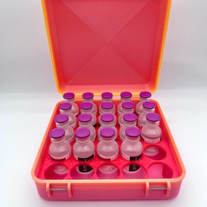 May include: A bright pink and orange plastic case with a hinged lid, containing 20 small clear glass vials with purple caps. The vials are arranged in a grid pattern within the case.