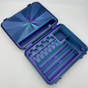 May include: A blue and purple hard case with a geometric pattern on the lid. The case has multiple compartments for storing small items, including a long, narrow compartment for storing a rolling paper.