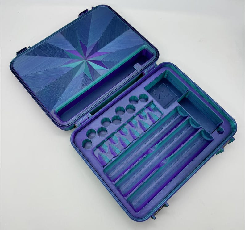 May include: A blue and purple hard case with a geometric pattern on the lid. The case has multiple compartments for storing small items, including a long, narrow compartment for storing a rolling paper.