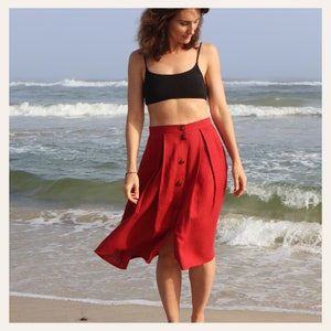 May include: A red linen skirt with a button-up front and a slit in the front. The skirt is pleated and has a high waist.