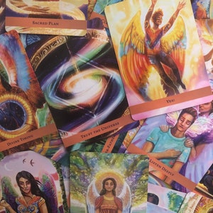 May include: A collection of oracle cards with colorful illustrations of angels and celestial imagery. The cards feature phrases like "Sacred Plan", "Trust the Universe", "Divine Timing", "Yes!" and "Listen Deeply".