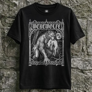 Black shirt hanging on a rustic hanger against a weathered stone wall, featuring a detailed gothic illustration of a werewolf beneath a full moon, framed by medieval cathedral-inspired architecture and rendered in a vintage engraving style.