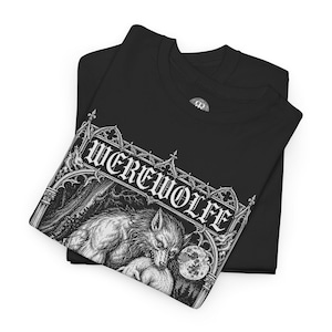 May include: A black t-shirt featuring a white graphic print of a werewolf under a full moon, framed by gothic architectural elements. The text 'WEREWOLFE' is printed in a stylized gothic font above the illustration, which depicts a forest scene.