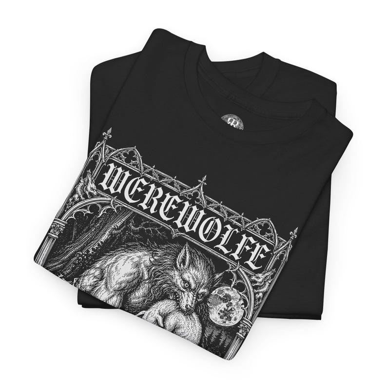 May include: A black t-shirt featuring a white graphic print of a werewolf under a full moon, framed by gothic architectural elements. The text 'WEREWOLFE' is printed in a stylized gothic font above the illustration, which depicts a forest scene.