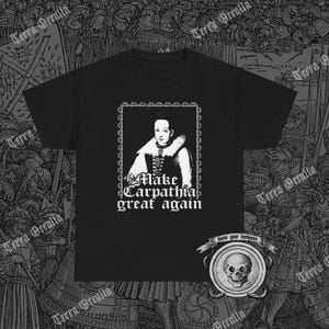 Op de afbeelding: Zwart T-shirt met een wit portret van een vrouw in een ingelijst beeld. De tekst "Make Carpathia great again" is onder de afbeelding gedrukt. Het T-shirt heeft een kleine schedelgrafiek in de rechterbenedenhoek met de tekst "Know your darkness".