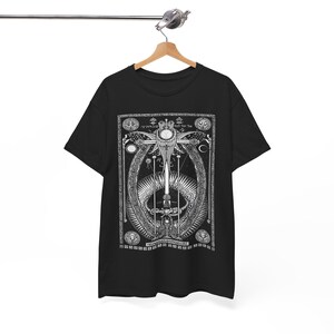 May include: Black t-shirt with a white graphic print of a sword surrounded by a circle of symbols and text. The graphic is centered on the shirt.
