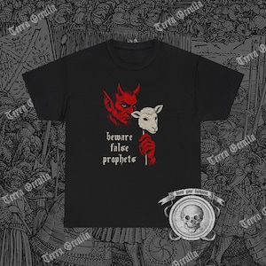 May include: Black t-shirt featuring a red devil and a lamb's head on a stick. The text "beware false prophets" is printed below the images. The shirt has a crew neck and short sleeves.