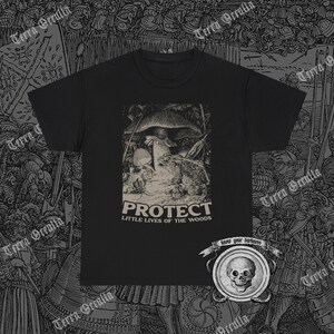 May include: Black t-shirt with a graphic print featuring a toad, mushroom, and skull scene. The word "PROTECT" is printed above "LITTLE LIVES OF THE WOODS". The shirt has a crew neck and short sleeves.