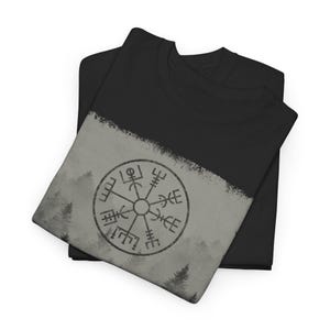 Może przedstawiać: Czarny t-shirt z szarym i białym wzorem przedstawiającym kompas na tle lasu.