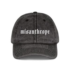 Op de afbeelding: Een donkergrijze baseballcap in vintage-stijl met het woord "misanthrope" in het wit geborduurd. De cap heeft een gebogen klep en een klassiek zes-panelen ontwerp.