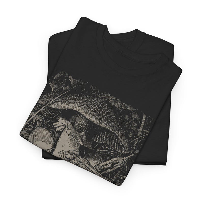 May include: Two black t-shirts are neatly folded and stacked. The top shirt features a detailed, sepia-toned graphic print of a fish and other aquatic elements. The design is reminiscent of an antique engraving. The shirts are made of a soft material.