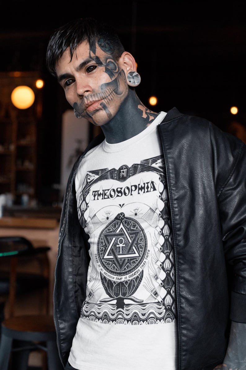 May include: A man with black and white tattoos, including a skull on his face, is wearing a white t-shirt with a black and white graphic design that says "Theosophia" and a black leather jacket.