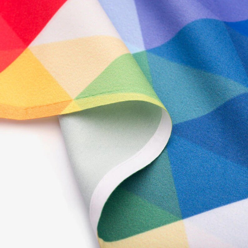 Pu&ograve; includere: Un tessuto con un motivo geometrico a triangoli in colori vivaci tra cui rosso, giallo, verde, azzurro e blu scuro. Il materiale &egrave; piegato per mostrare un bordo bianco rifinito e una consistenza superficiale liscia e opaca.