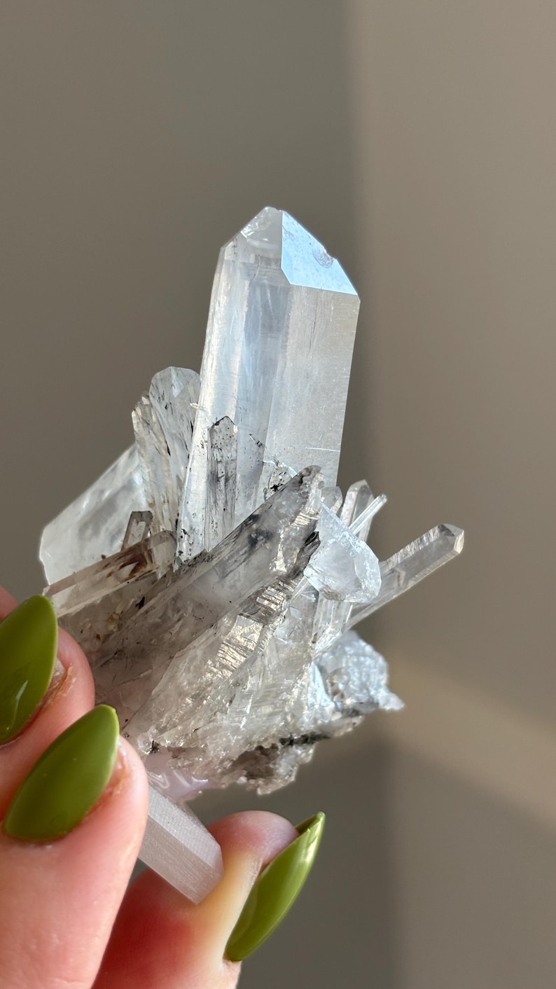 May include: A cluster of clear quartz crystals with sharp, pointed ends. The crystals are translucent with some internal inclusions. The overall shape is irregular, with multiple crystal points radiating outwards. The quartz is a pale, almost colourless hue.