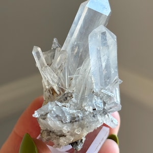 May include: A collection of clear quartz crystals, displaying multiple points and a crystalline structure. The quartz is mounted on a small, clear, rectangular base. The crystals vary in size, with some appearing larger and more defined than others.