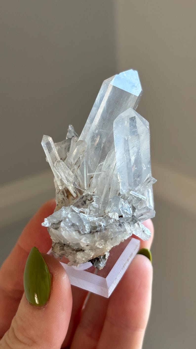 May include: A collection of clear quartz crystals, displaying multiple points and a crystalline structure. The quartz is mounted on a small, clear, rectangular base. The crystals vary in size, with some appearing larger and more defined than others.