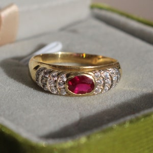 Peut inclure: Une bague en or avec une pierre rouge entourée de petites pierres blanches.