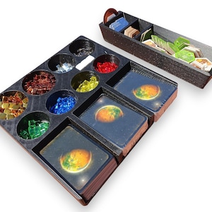 May include: A wooden board game organizer with compartments for game pieces and cards. The organizer has various colored game pieces, including gold, red, blue, and green. The cards have a planet design. A separate tray holds additional game components.