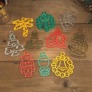 May include: A set of ten Christmas ornaments in various colors and designs, including a palm tree, a Christmas tree, a snowman, a bell, a nutcracker, a gingerbread house, a lantern, a mug of hot chocolate, and a snowflake. The ornaments are made of plastic and have a 3D design.