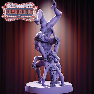 Puede incluir: Una escultura morada de un acto de circo zombi. Tres figuras están apiladas, realizando un acto de equilibrio. La figura superior está boca abajo. La escultura está sobre una base redonda. El texto "ZOMBICIRCUS" está encima.
