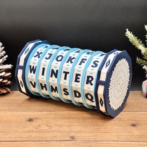 May include: A blue and white wooden puzzle with the word "WINTER" spelled out. The puzzle has a cylindrical shape with rotating rings and geometric designs on the ends. The letters are in black, and the background is light blue.