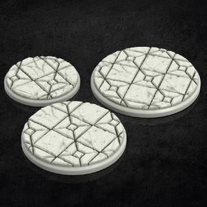 May include: Three white, circular gaming bases with a textured, geometric pattern. The bases are of varying sizes, with a raised, rounded edge. The surface has a cracked stone appearance, ideal for miniature figures.