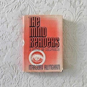May include: A vintage paperback book titled "The Mind Readers" by Margery Allingham. The cover is red with black text and a white eye graphic. The book is a novel of suspense.