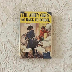 Puede incluir: Una portada de libro vintage con el título "The Abbey Girls Go Back To School". La portada presenta una ilustración de tres chicas en una habitación de dormitorio, con una chica sosteniendo una almohada.