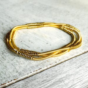 Puede incluir: Un conjunto de pulseras doradas. Las pulseras están hechas de alambre fino enrollado y tienen un diseño simple y elegante. Las pulseras están apiladas, creando un aspecto en capas. El color dorado da a las pulseras una sensación lujosa.