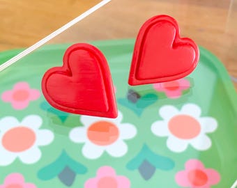 May include: Two bright red heart-shaped objects are positioned on a green tray with a floral pattern. The tray is partially visible behind a clear, angled surface. The hearts are the focal point, with a glossy finish, and the tray's design adds a playful touch.