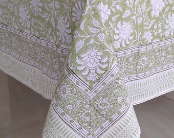 May include: A green and white floral tablecloth. The tablecloth features a repeating pattern of large white flowers and leaves on a light green background. The border has a detailed design with geometric and floral elements.