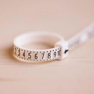 May include: White plastic ring sizer with black numbers 2 to 10.