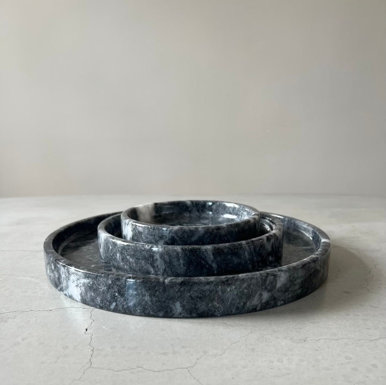 May include: Three round marble trays in different sizes, nested together. The trays are black with white veining.