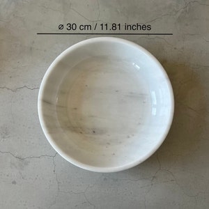 May include: White marble bowl with a diameter of 11.81 inches. The bowl is smooth and has a subtle gray veining pattern.