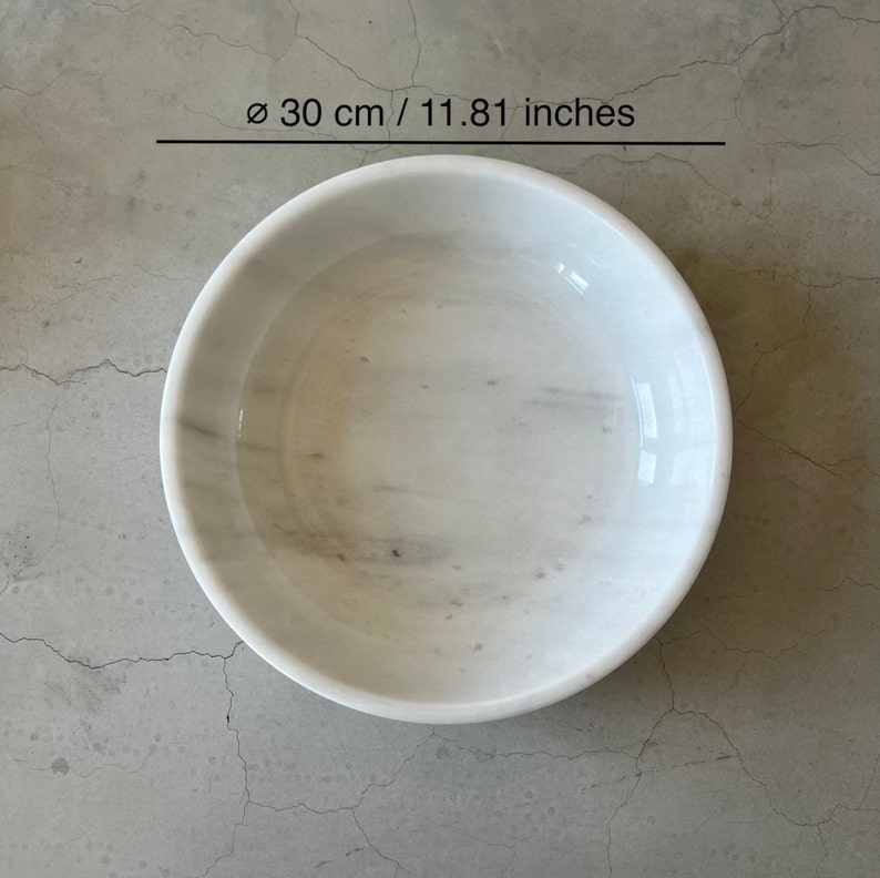 May include: White marble bowl with a diameter of 11.81 inches. The bowl is smooth and has a subtle gray veining pattern.