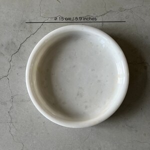 Pode incluir: Tigela de m&aacute;rmore branco com um di&acirc;metro de 15 cm ou 5,9 polegadas. A tigela &eacute; redonda e tem uma superf&iacute;cie lisa.