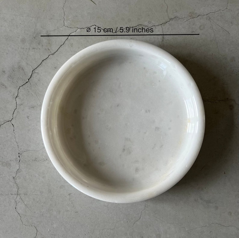 Pode incluir: Tigela de m&aacute;rmore branco com um di&acirc;metro de 15 cm ou 5,9 polegadas. A tigela &eacute; redonda e tem uma superf&iacute;cie lisa.