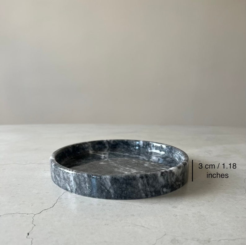 May include: A round, gray marble trinket tray with a white marbled pattern. The tray is 3 cm / 1.18 inches in diameter.
