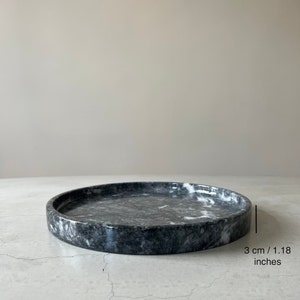 May include: A round, gray marble tray with white veining. The tray is 3 inches in diameter.